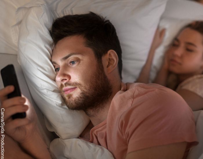 Foto de uno de los signos del zodiaco más infieles mirando el celular mientras su esposa duerme