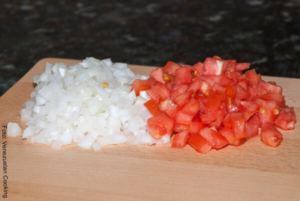 Foto de cebolla y tomate picados en cuadritos sobre una tabla de picar