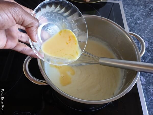 Foto de la mano de una mujer añadiendo yemas de huevo en leche