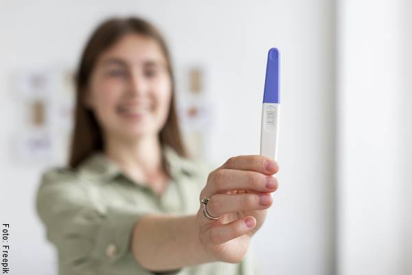 Foto de una mujer sonriente con una prueba de embarazo en su mano