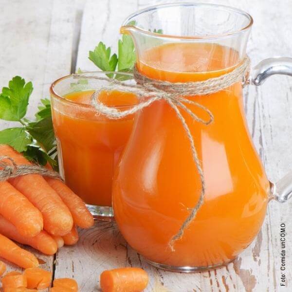Foto de batido de naranja con zanahoria en una jarra y un vaso de vidrio