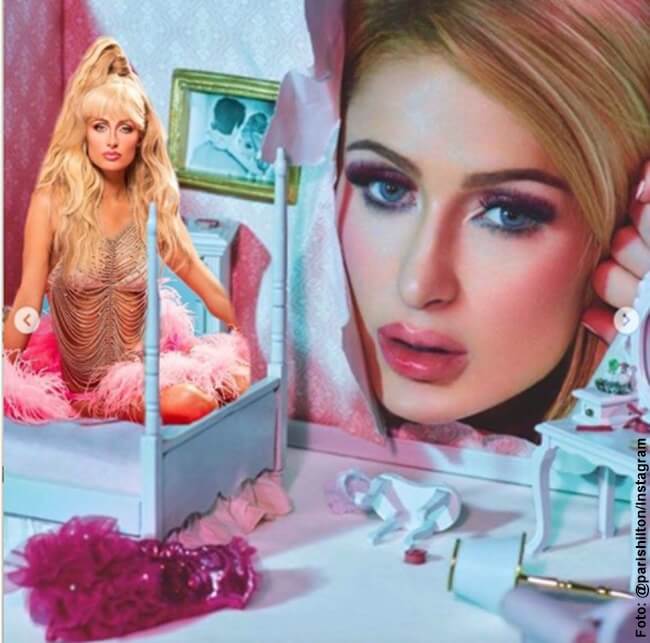 Foto de Paris Hilton sentada en una pequeña cama de Barbie delante de un afiche de su propio rostro