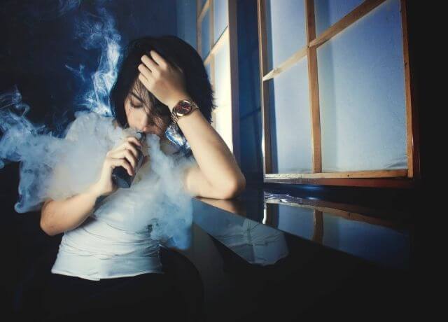 Foto de una mujer bebiendo de una botella y rodeada de humo