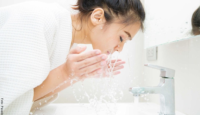Foto de una mujer lavándose la cara con agua tibia