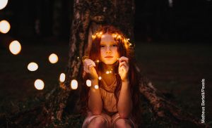 Foto de niña sentada en el bosque sosteniendo unos bombillos