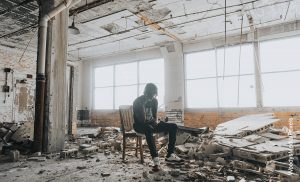 Foto de un hombre sentado entre ruinas de una casa