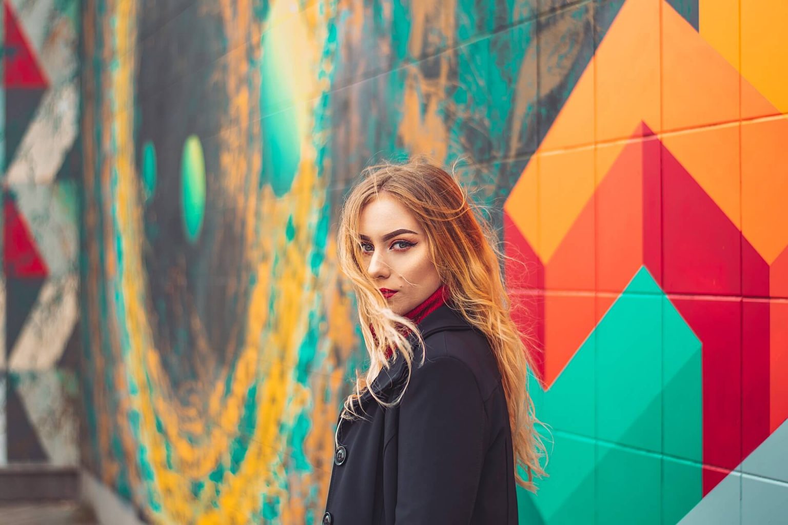 Foto de una mujer rubia posando frente a un mural de colores