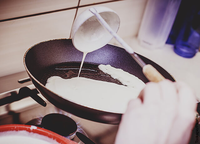 Foto de cuchara que vierte mezcla sobre sartén que muestra cómo hacer pancakes