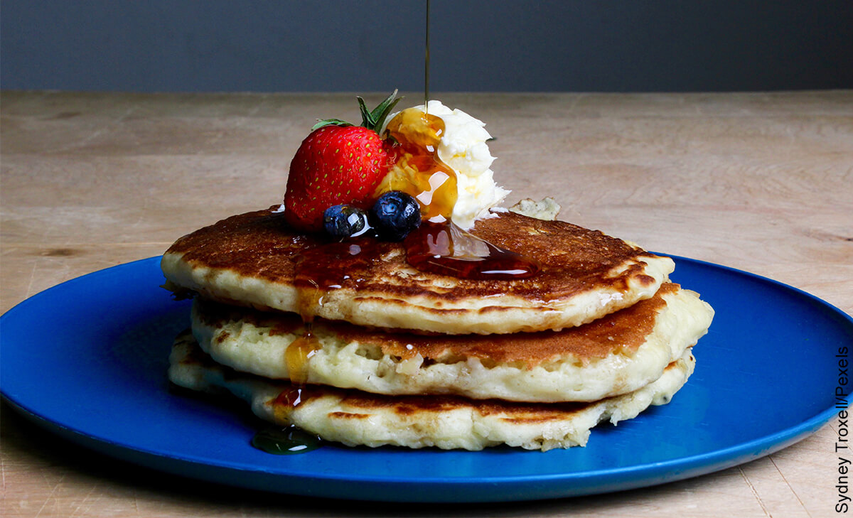 Foto de un plato de pancakes con fruta, crema y miel