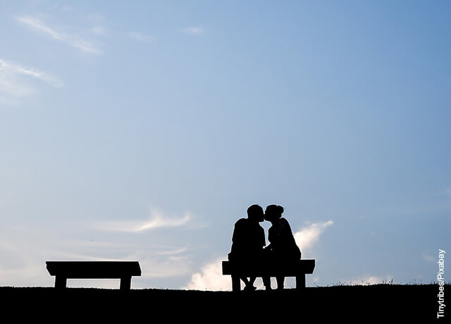 Foto de una pareja de novios besándose en una banca de un parque