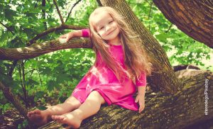 Foto de una niña sonriendo encima de una rama de árbol que ilustra los nombres de niña