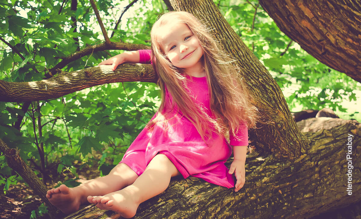 Foto de una niña sonriendo encima de una rama de árbol que ilustra los nombres de niña
