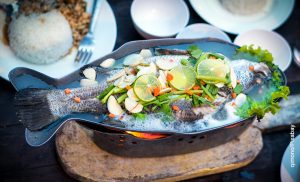 Foto de un pescado guisado con verduras por encima sobre un plato que muestra para qué sirve la proteína