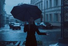 Foto de una mujer vestida de negro bajo un aguacero que ilustra lo que significa soñar con lluvia