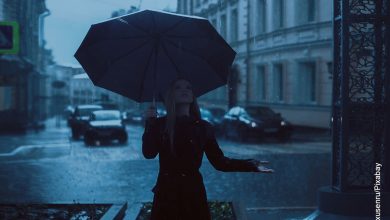 Foto de una mujer vestida de negro bajo un aguacero que ilustra lo que significa soñar con lluvia