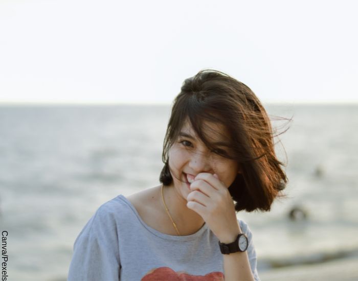 Foto de una mujer de signo de aire sonriendo en la playa con el viento en la cara