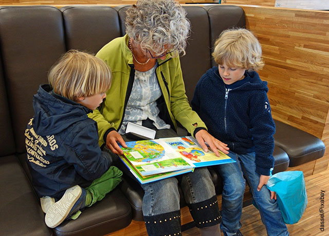 Foto de dos niños con su abuela leyendo en el sofá