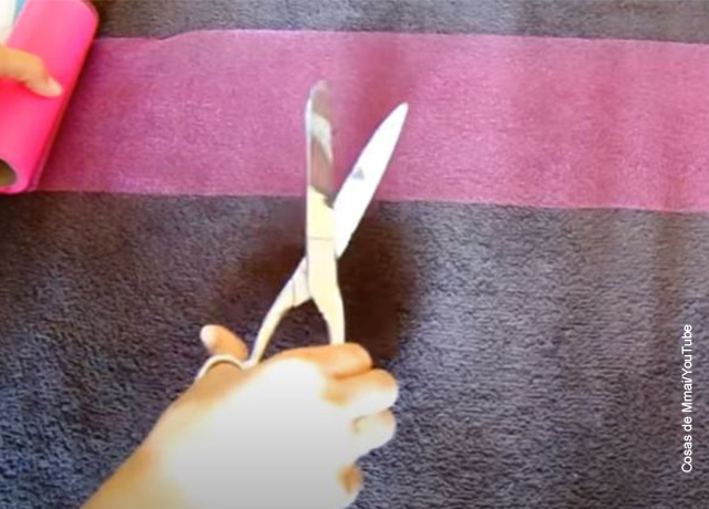 Foto de una mano con una tijeras cortando tela
