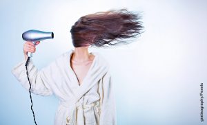 Foto de una mujer usando una secadora de cabello mientras se despeina