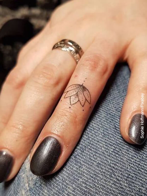 Foto de la mano de una mujer con un tatuaje de flor de loto en sus dedos