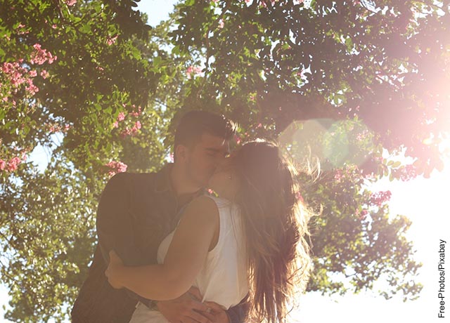 Foto de un hombre y una mujere dándose un beso bajo un árbol