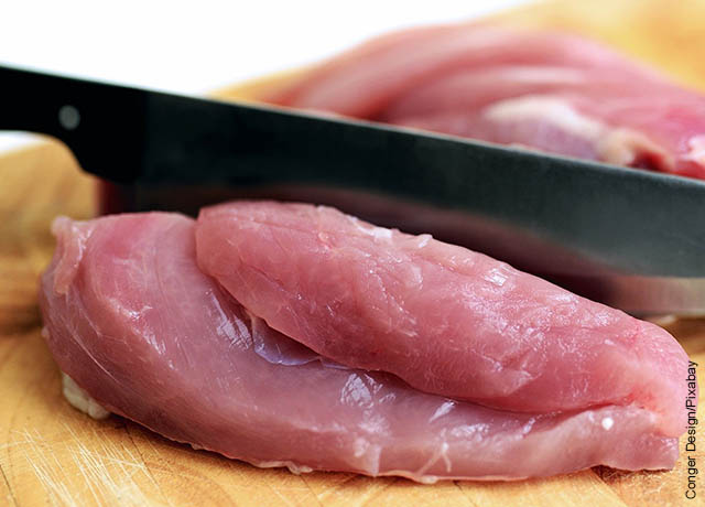 Foto de un cuchillo cortando pollo crudo