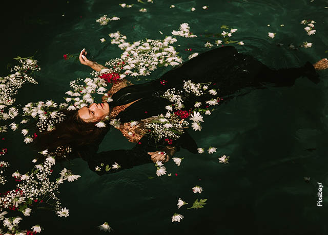 Foto de una mujer flotando en el agua con pétalos de rosa