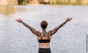 Foto de una mujer practicando yoga frente a un lago que ilustra los tatuajes en la espalda