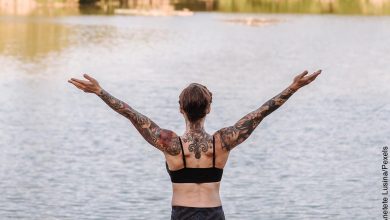 Foto de una mujer practicando yoga frente a un lago que ilustra los tatuajes en la espalda