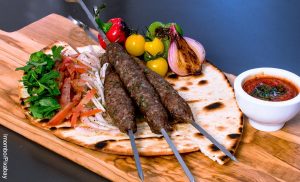 Foto de pinchos, una pan y vegetales sobre una tabla de madera que muestra la comida árabe y sus recetas
