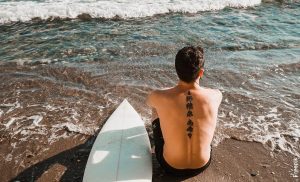 Foto de un hombre sentado con una tabla de surf a la orilla del mar
