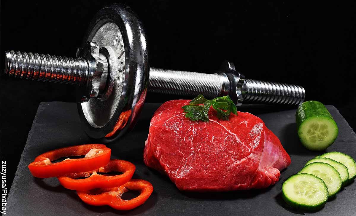 Foto de una pesa junto con un trozo de carne cruda, pimeones y pepino que revela qué comer antes de hacer ejercicio