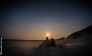 Foto de dos personas sentadas en la playa viendo el atardecer que muestra qué preguntas hacerle a una mujer