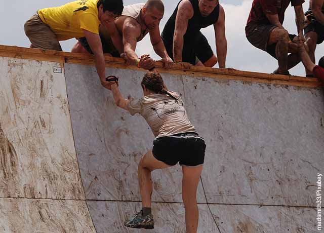 Foto de varias personas ayudando a una mujer a subir una pared