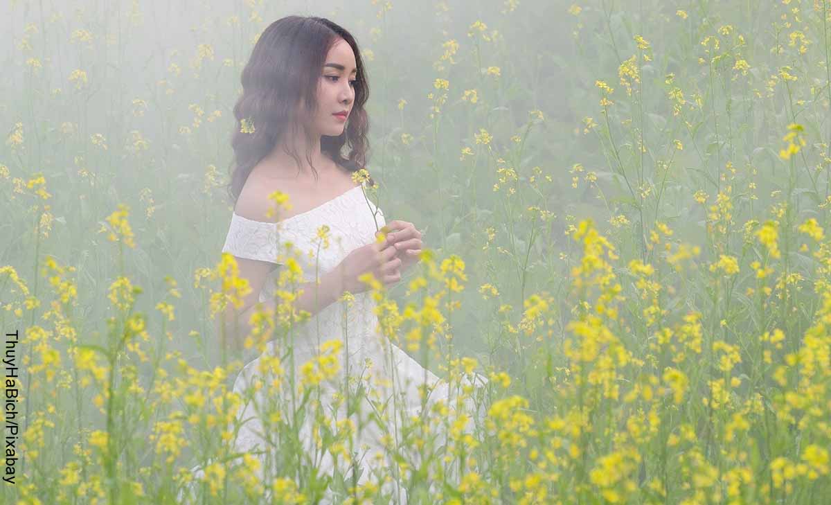 Foto de una mujer caminando entre plantas amarillas que muestra lo que es soñar con vestido blanco