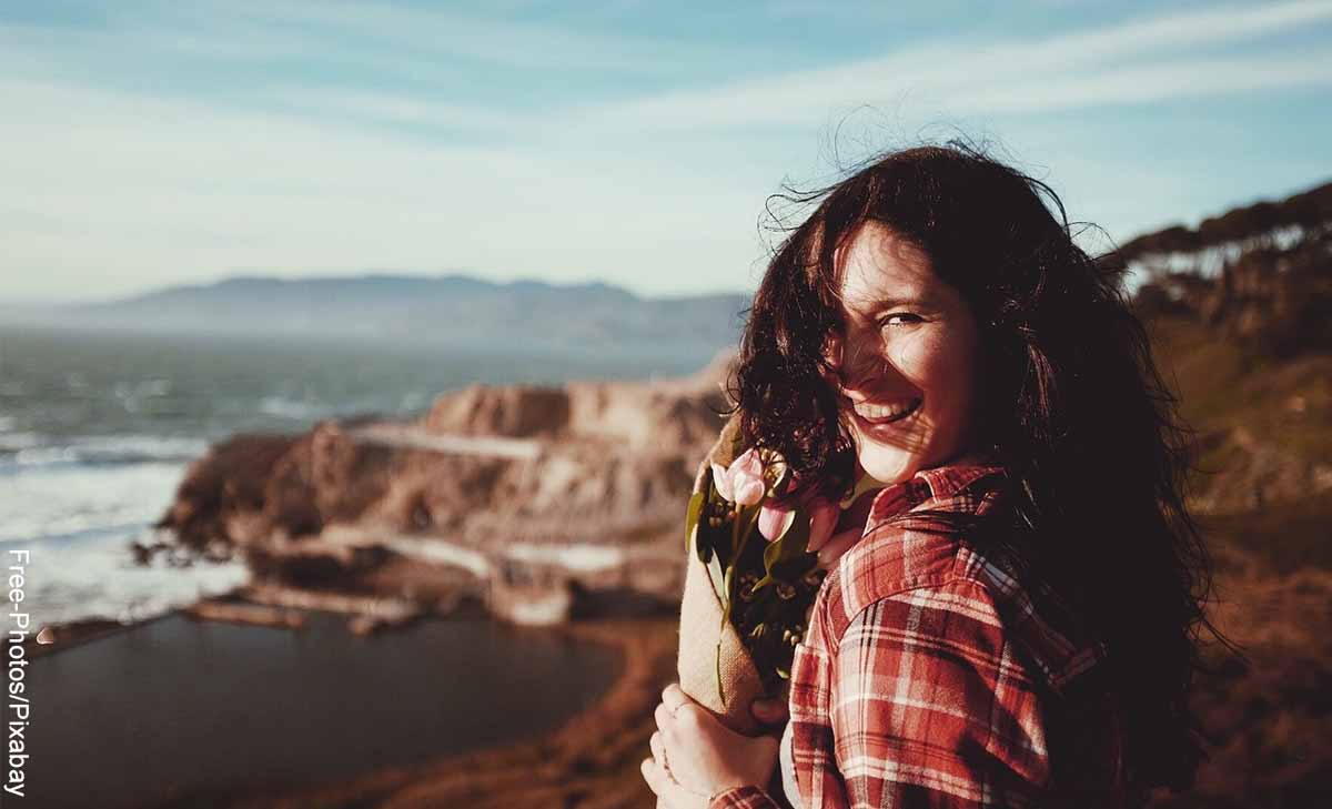 Foto de una mujer feliz y sonriendo en la playa que revela la biotina para qué sirve