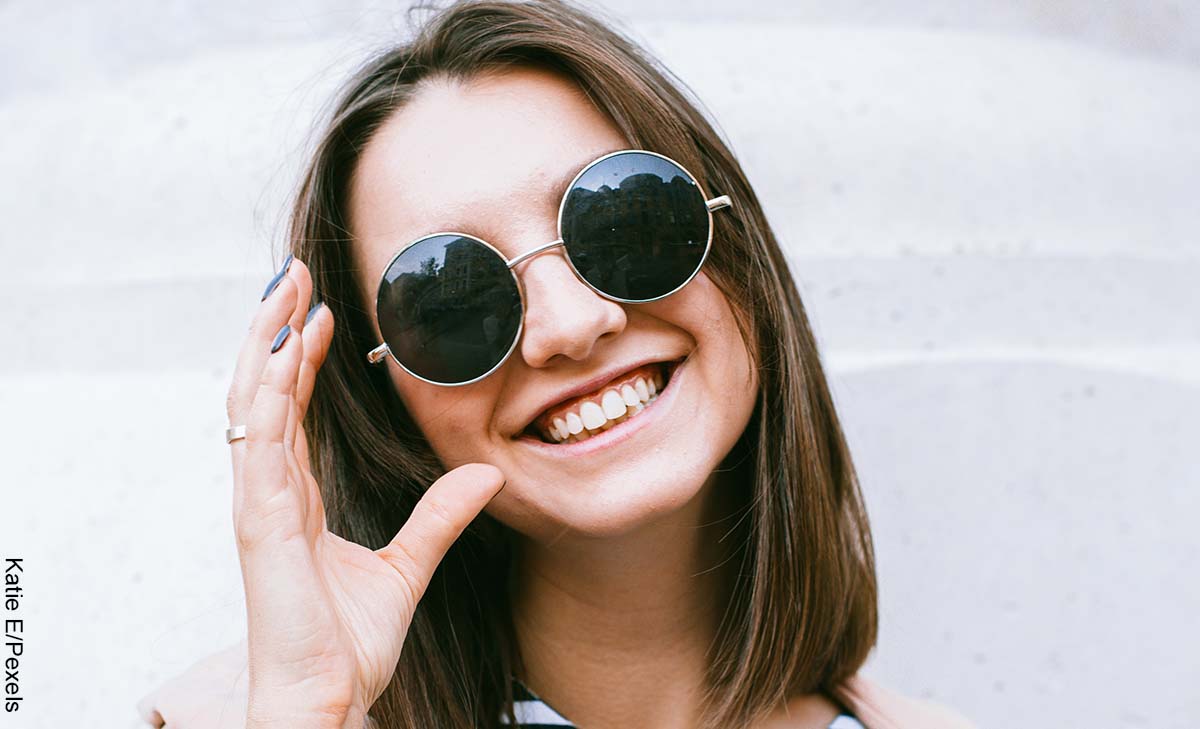 Foto de una mujer joven de pelo corto sonriendo con gafas oscuras puestas y que revela las imágenes de cortes de cabello