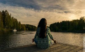 Foto de una mujer sentada en un muelle frente a un lago que muestra para qué sirve la meditación