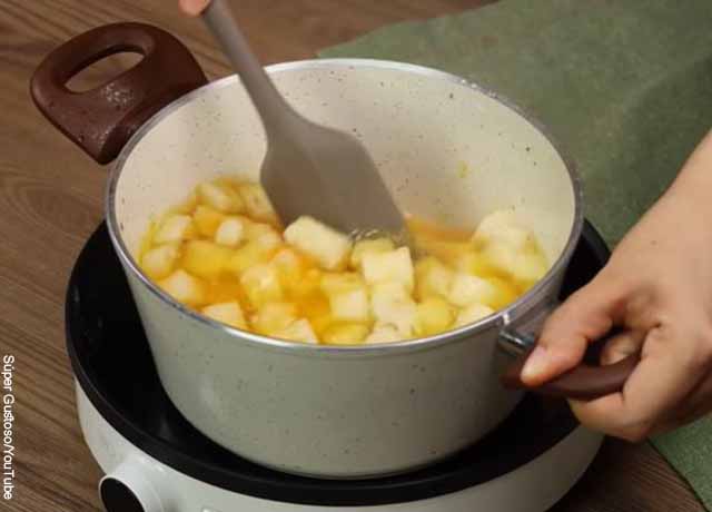 Foto de una mano mezclando piña en una olla