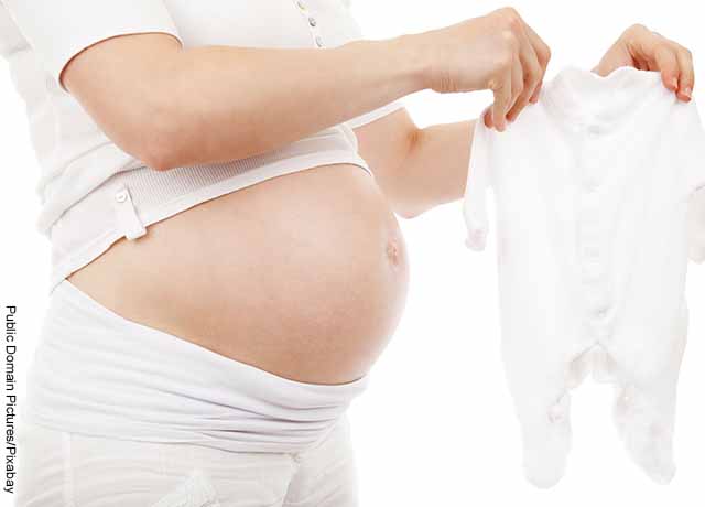 Foto de una mujer embarazada que extiende ropa de bebé