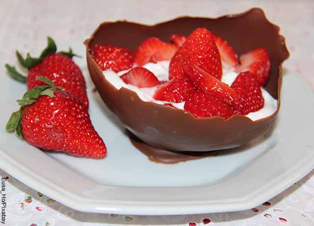 Foto de un postre de fresas con crema servido en un trozo de chocolate