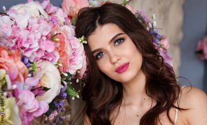 Foto del rostro de una mujer joven entre flores que revela para qué sirve el colágeno
