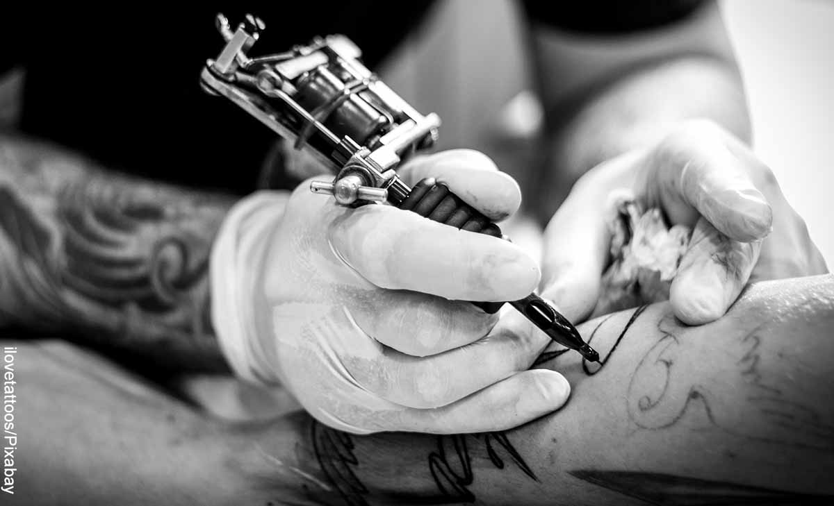 Foto de una mano con una máquina de tatuar que muestra el significado de los tatuajes de plumas para mujeres