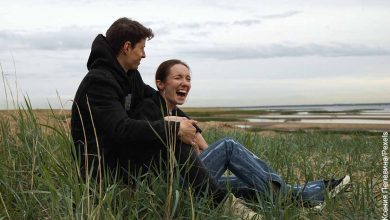 Foto de una pareja riendo sentada en un paisaje que revela las cosas para hacer en pareja