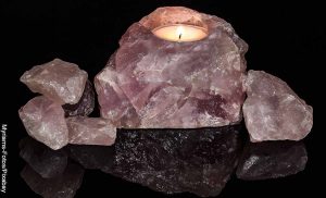 Foto de una piedra mineral rosada con una vela que muestra el significado de los cuarzos