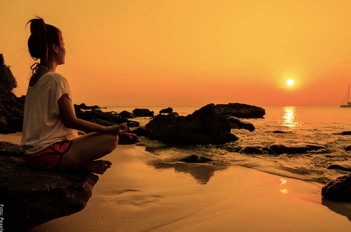 Foto de una mujer meditando sobre una roca frente al atardecer frente al mar