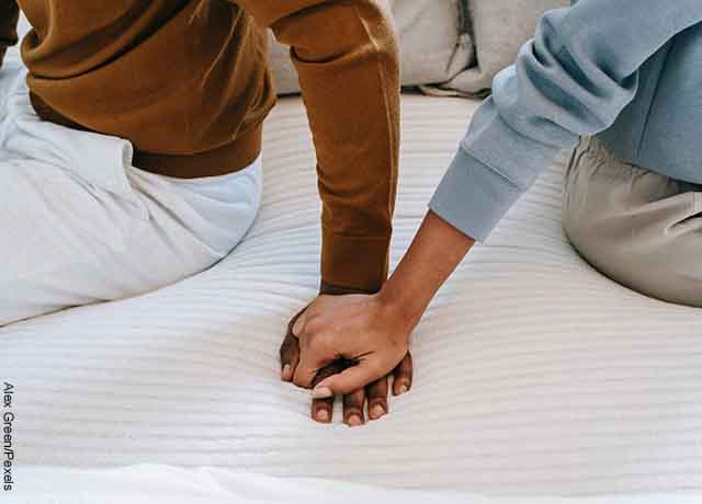 Foto de una pareja con las manos agarradas sobre una cama
