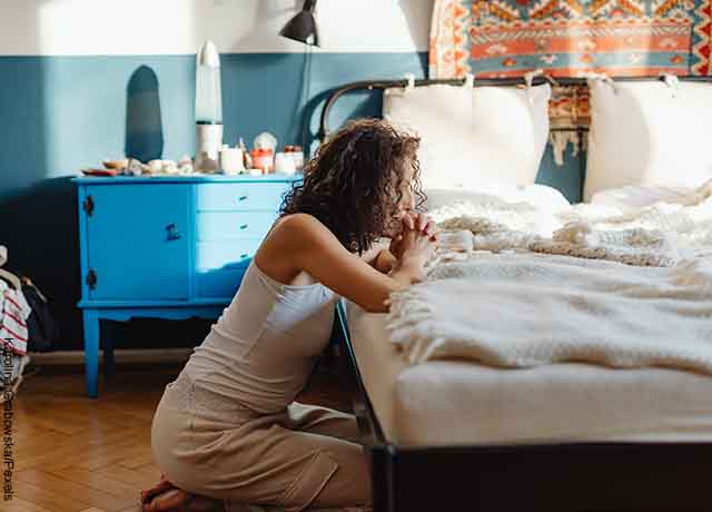 Foto de una mujer orando al lado de su cama