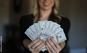 Foto de una mujer sonriendo con billetes en la mano que revela qué significa soñar con encontrar dinero