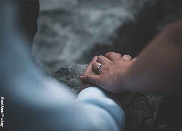 Foto de una pareja tomada de la mano que revela lo que es soñar con anillo de compromiso
